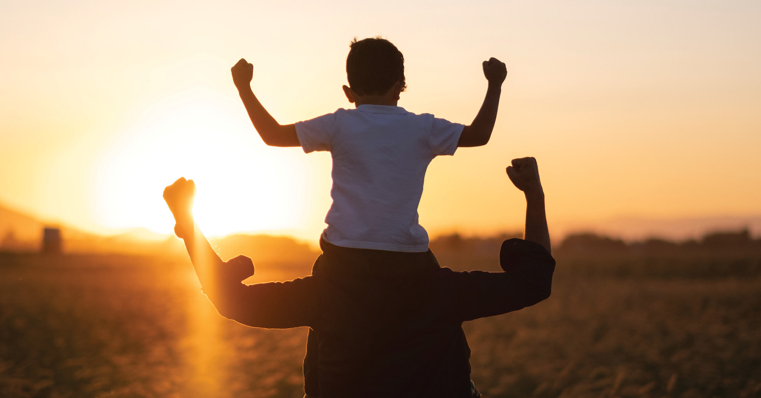 Child on father's shoulders with arms raised.